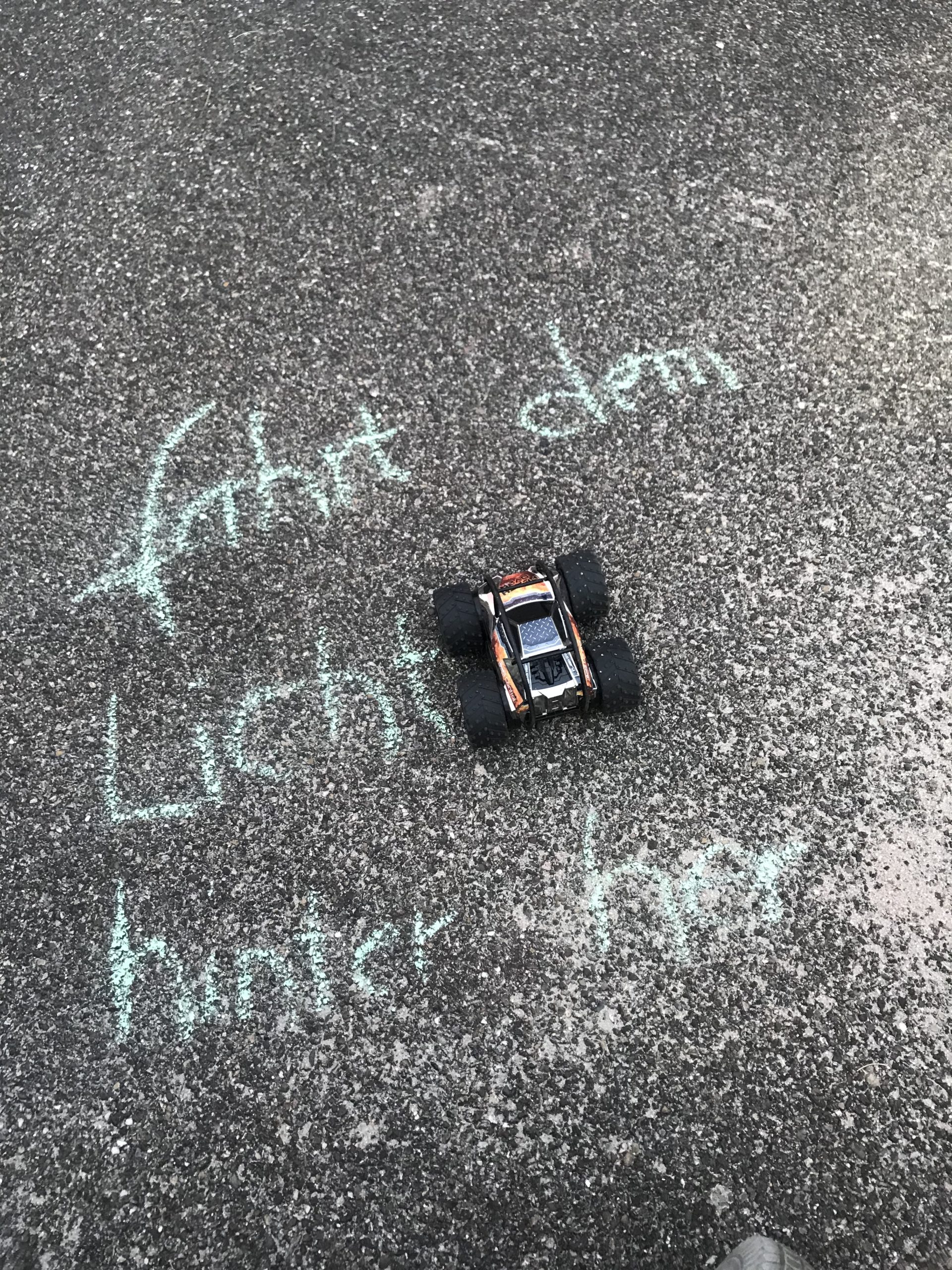 Ein Spielzeugauto und auf dem Boden mit Starßenkreide die Anweisung: Fahrt dem Licht hinterher 