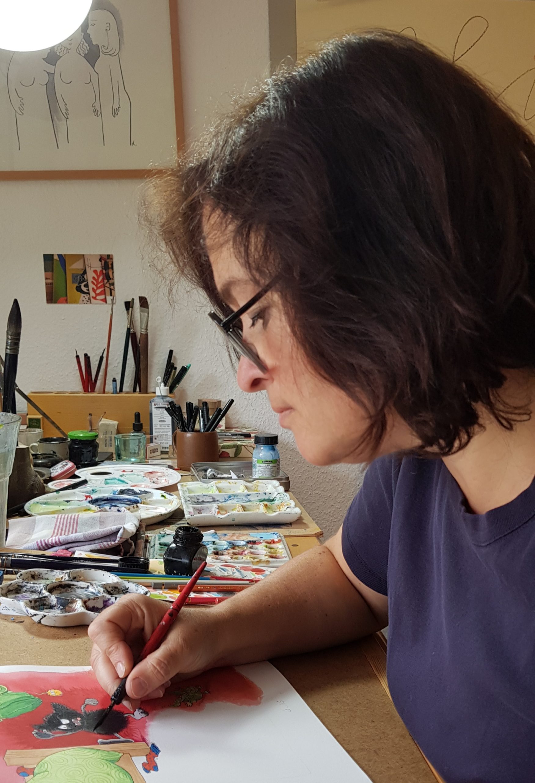 Franzsika sitzt mit Brille im Atilier und zeichnet an einem MUffelmonster. Sie ist von der Seite fotografiert und scahut konzentriert auf den Stift in ihrer Hand