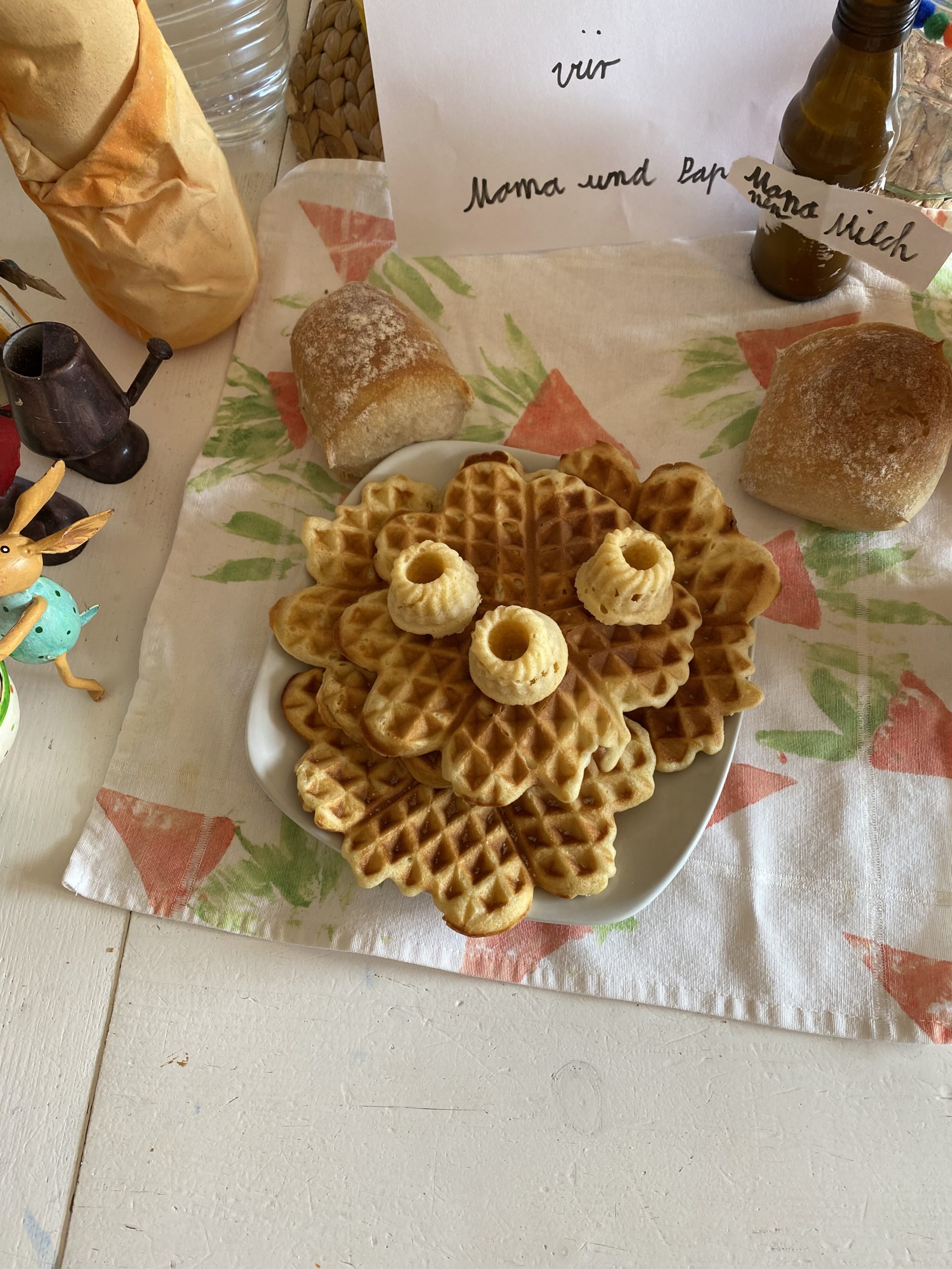 Ein Teller mit Waffeln, kleinen Minigugelhupf, Banenenmilch und Osterdeko auf demTisch 