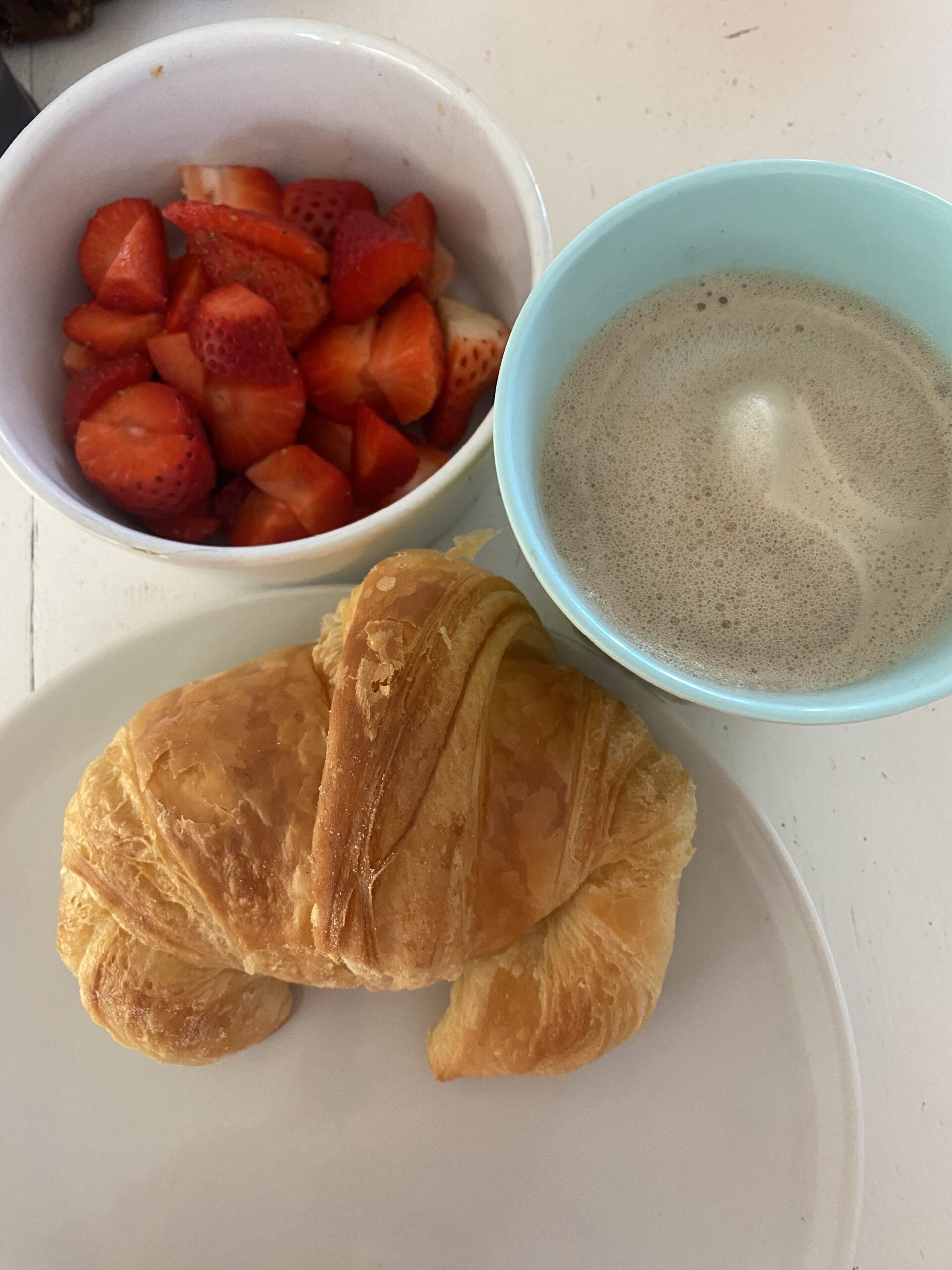Ein Bild mit Cafe rechts oben, davor ein Corossaint und links oben einer Schale Erdbeeren