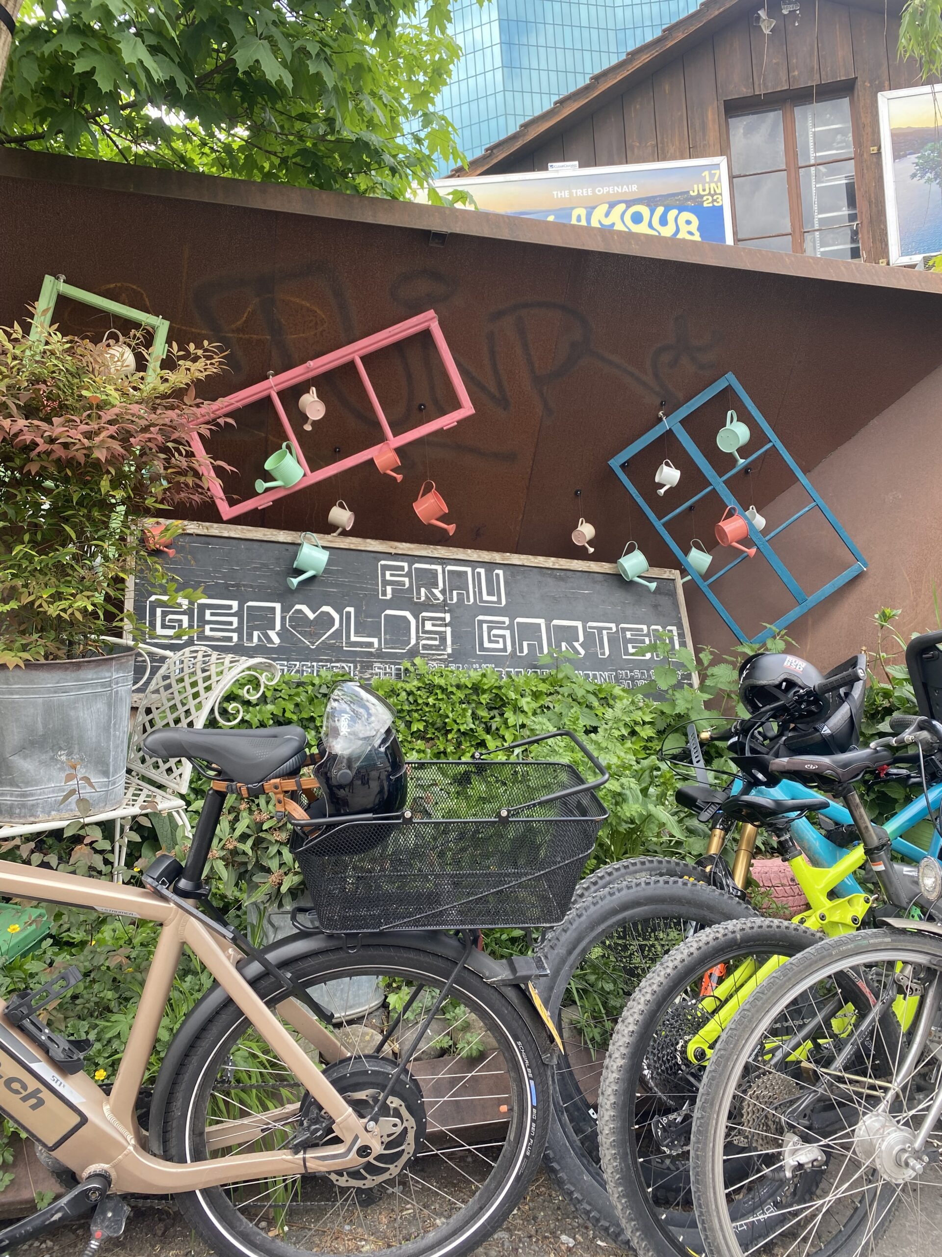 Fahrräder, alte Fensterrahmen und ein großes Schild Frau Gerolds Garten