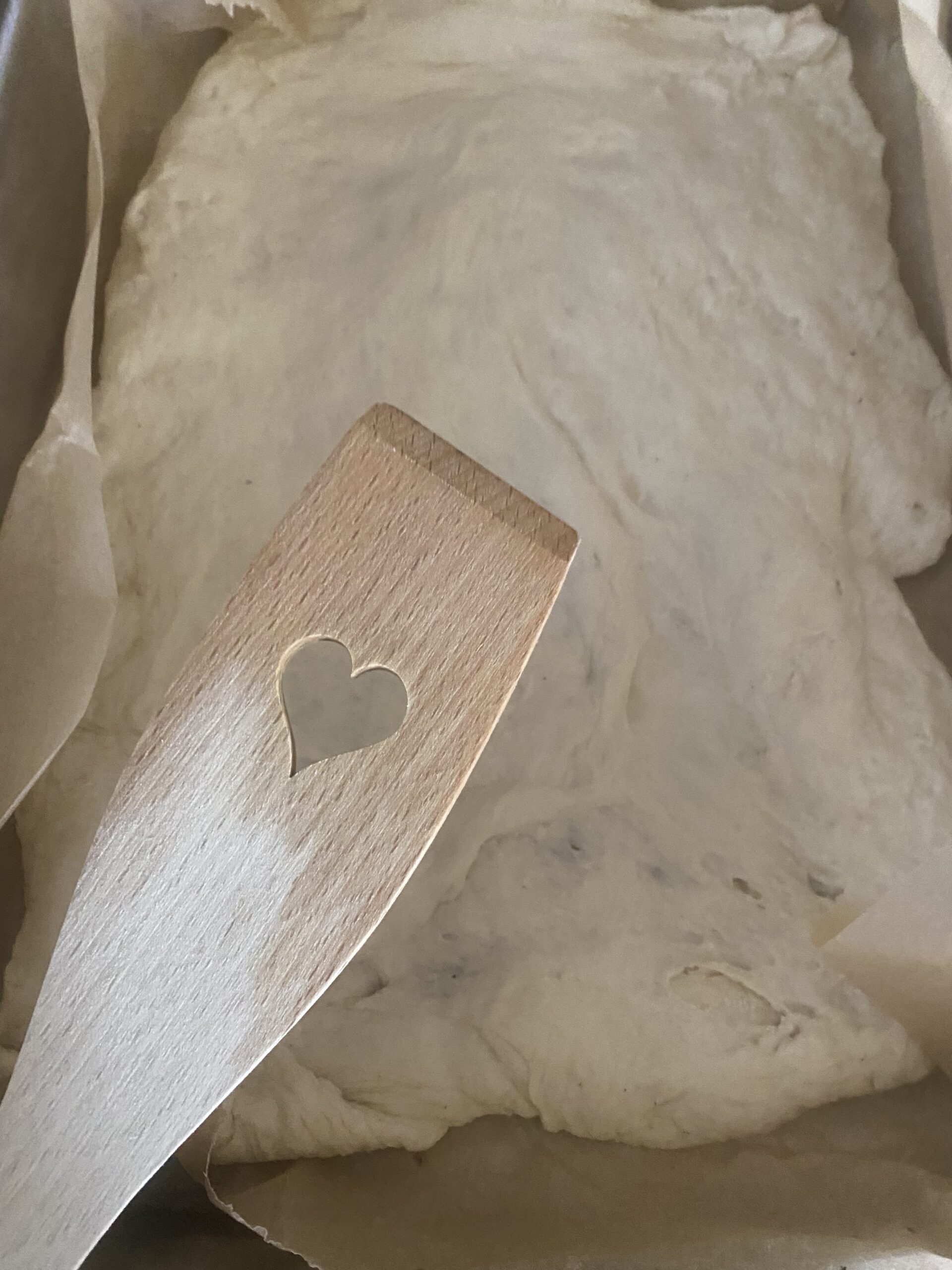Teig in einer Form mit einem Kochlöffel mit einem Herz in der Mitte 